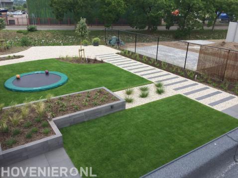 Moderne tuin met kunstgras en grindpad met stapstenen van natuursteen